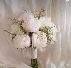 a bridal bouquet with white peonies and baby's breath on a bed