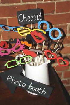 a cup filled with lots of different colored scissors on top of a wooden table next to a brick wall