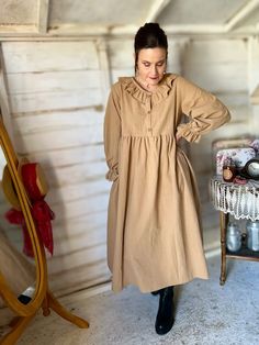 a woman standing in front of a mirror wearing a tan dress and black boots with her hands on her hips