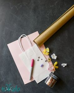 a paper bag, pen, and flower on a table next to some gold foil