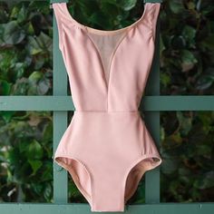 a pink one piece swimsuit hanging on a green fence with greenery in the background