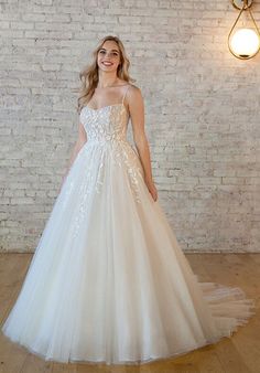 a woman in a white wedding dress standing on a wooden floor next to a brick wall