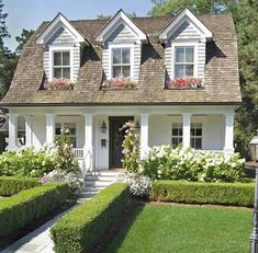 a white house surrounded by hedges and flowers