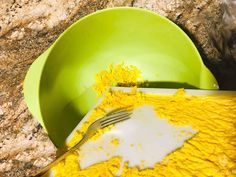 a green bowl filled with yellow food next to a knife and fork on top of a counter