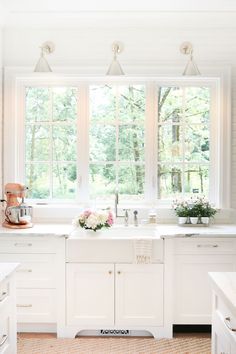 a white kitchen with lots of windows and flowers on the sink counter top in front of it