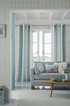 a living room with blue and white curtains on the windowsills, a gray couch and coffee table in front of it