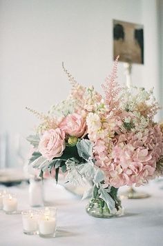 a vase filled with pink and white flowers on top of a table next to candles