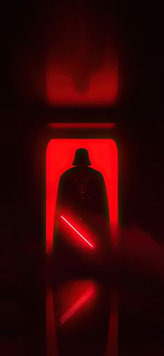 a darth vader silhouetted against a red light in a dark room with the lights on