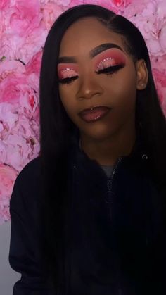 a woman with long black hair and bright pink eyeshadow is posing in front of flowers