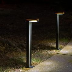 two metal poles are lit up at night on the side of a sidewalk with grass