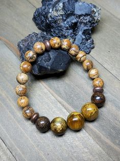 two bracelets with tiger's eye beads are sitting on a wooden table next to a rock