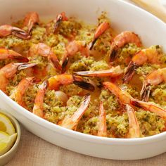 a white dish filled with shrimp and broccoli covered in sauce next to some bread