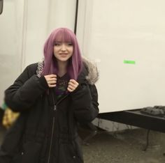 a young woman with pink hair standing in front of a trailer