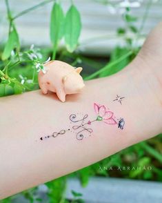 a small pig tattoo on the arm with flowers and butterflies around it, sitting next to a plant