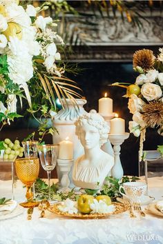 a table topped with white flowers and candles next to a vase filled with greenery