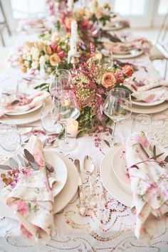 the table is set with white plates and pink napkins, silverware, and flowers