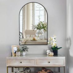 a mirror on the wall above a table with flowers and other items in front of it