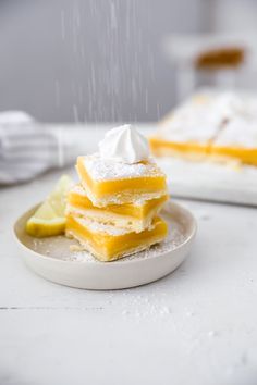 a stack of lemon bars on a white plate with whipped cream and lime wedges