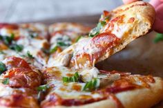 a person taking a slice of pizza from a wooden cutting board on top of a table