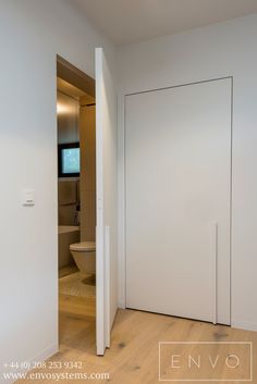 an empty bathroom with white walls and wood flooring is seen from the doorway to the toilet