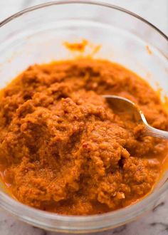 a glass bowl filled with sauce on top of a marble counter next to a metal spoon