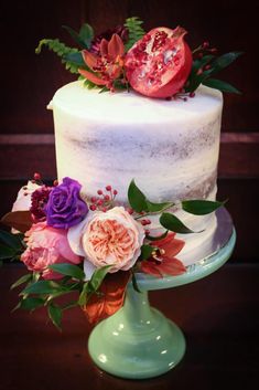 a white cake with flowers and pomegranates is on a green pedestal