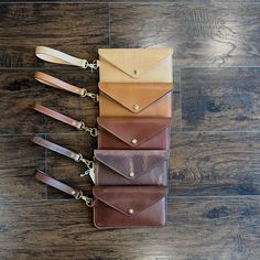 four leather wallets are lined up on a wooden floor, one is brown and the other is tan