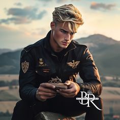 a young man sitting on top of a rock looking at his cell phone with mountains in the background