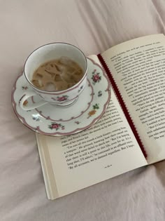 an open book with a cup of coffee on top of it next to a teacup and saucer