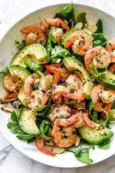 a white bowl filled with shrimp, avocado and spinach salad on top of a marble table