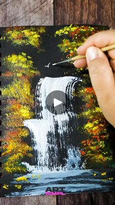 someone is painting a waterfall with watercolors on the paper and holding a pencil