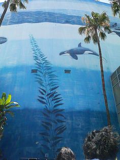 two people are standing in front of a mural with dolphins and plants on the side