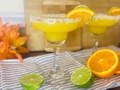 two margarita cocktails with orange slices and sugar on the rim, garnished with lime