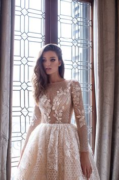 a woman standing in front of a window wearing a dress with long sleeves and lace detailing