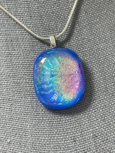 "Oval Dichroic pendant with multiple layers of dichroic. The base is a beautiful Periwinkle Blue (Lavender) with a rainbow dichroic layer. The top layer is a holographic style dichroic  pattern in a shimmering green/gold. The silver plated leaf-shaped bail is adhered to the back. Snake chain shown is available separately. Bail opening is best fit for 1mm to 1.5mm chain diameters. All jewelry is hand-made by me in my home studio. Every piece has been fired multiple times with the proper annealing programs for strength and durability. Most items have been cold-worked one or two times and fire polished to finish the edges and to achieve the shape I had in mind.  Dichroic glass is produced by vaporizing metal oxides to the surface of either transparent or opal glass. After fusing, the glass ha Fused Glass Necklace, Dichroic Pendant, Silk Gifts, Dichroic Glass Pendant, Fused Glass Pendant, Blue Lavender, Glass Artwork, Glass Pendant Necklace, Glass Ideas