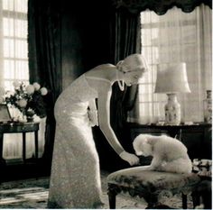 a woman in an elegant dress petting a poodle on the arm of a chair