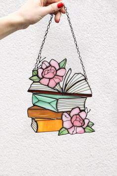 a hand holding a stained glass book with flowers hanging from it's front end