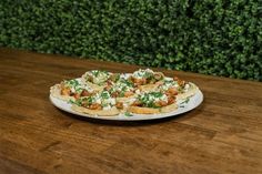 a white plate topped with food sitting on top of a wooden table next to a green hedge