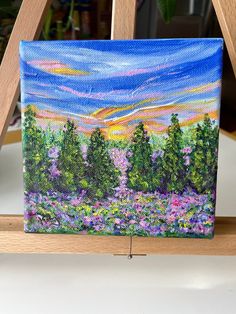 an acrylic painting of trees and flowers on a easel