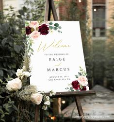 a welcome sign with flowers on it in front of some bushes and greenery at a wedding