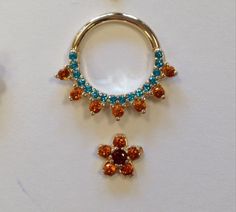 an orange and blue jeweled navel ring next to a pair of dangling earrings