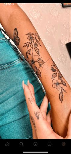 a woman's arm with flowers and butterflies on it, next to her hand