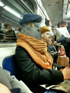 there is a bird wearing a hat and scarf on the subway train with people in the background