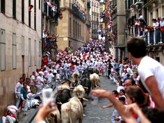 a group of people walking down a street next to bulls