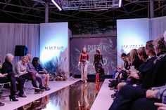 a woman is walking down the catwalk at a fashion show while people sit and watch