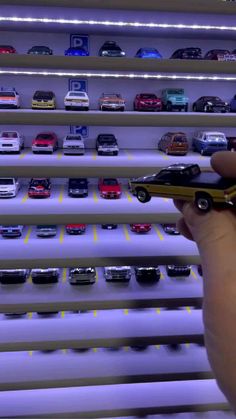 a person holding a toy car in front of a display case with cars on it