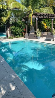 an empty swimming pool surrounded by trees and plants in a backyard with patio furniture on the side