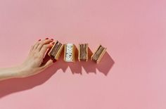 a woman's hand reaching for some sandwiches on a pink background by jodi lenski for stocksy photography