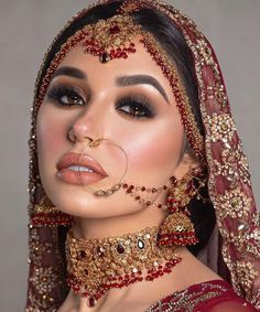 a woman wearing a red and gold bridal outfit with her nose ring in the middle