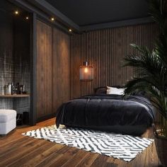 a bedroom with wood paneling and black bedding, white rugs and a palm tree in the corner